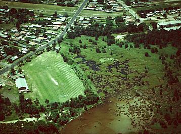 Aerial view of Marton Park, November 1999, showing Marton Hall, Stingrays Football clubhouse and oval, netball and tennis courts, playground, garden and the pre-school. A creek and wetlands surround the park.